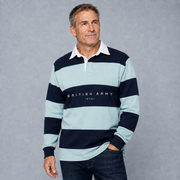 A man wearing a light blue and navy striped long-sleeve rugby shirt with 'BRITISH ARMY (RTD)' printed on the chest, paired with dark jeans, standing against a textured gray studio background.